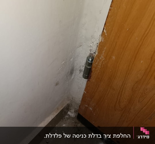 ציר מתכת בדלת עץ ליד קיר לבן